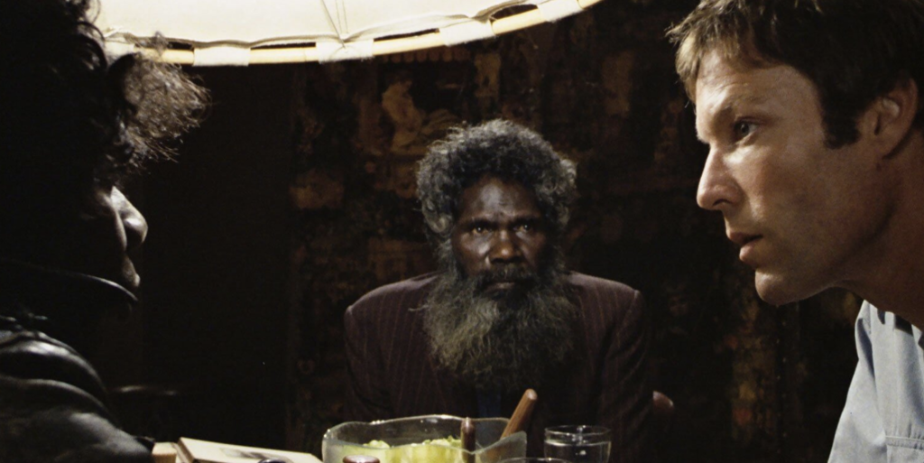 Three men sit around a table. The one on the left and the middle are Aboriginal men, the one on the right is a white lawyer.