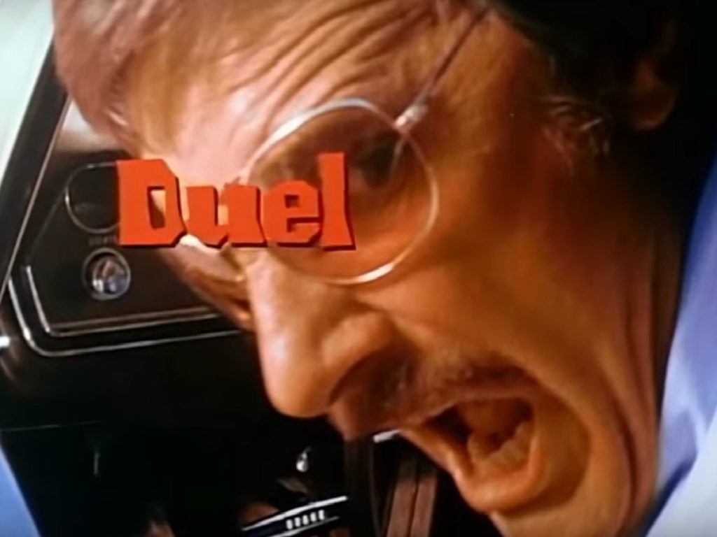 A screenshot from the Duel trailer shows David Mann in closeup, yelling over his shoulder. The movie’s title is layered in a red font over his eyes.