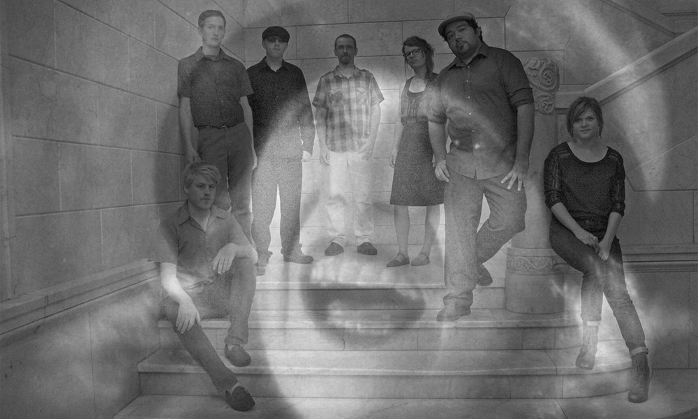 A double-exposed image of 1) the Poor Nobodys in a concrete stairway with a brick background for a press photo, six people dressed in casual clothes looking into the camera, four of them standing in the center and one member sitting down on either side, and 2) a close-up of a screaming woman with medium-length hair and a hat, mouth agape with horror, from the film The Lodger: The Story of the London Fog.