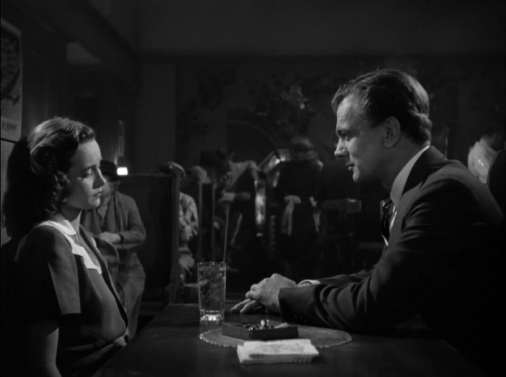 A young woman sits across from a man in a restaurant booth. She looks away from him while the man leans toward her