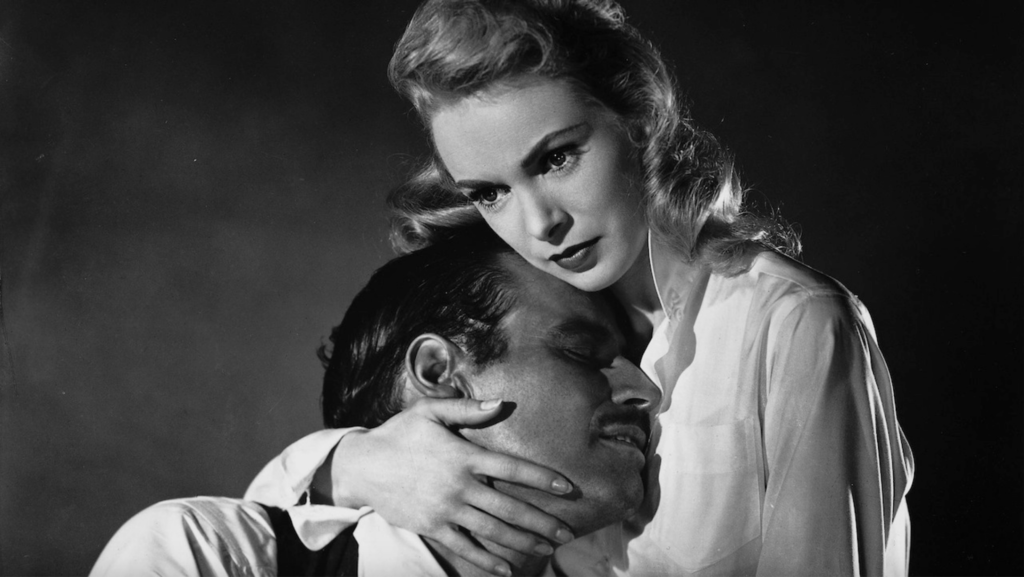 A man with a sleazy mustache (up to user interpretation) presses his head against the chest of a blonde woman, who looks off into the distance.