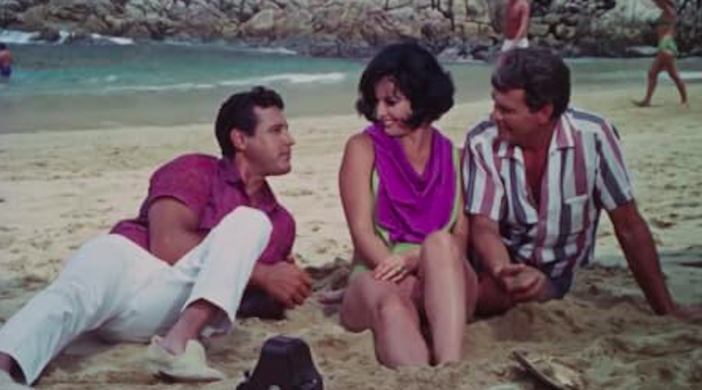 left to right, a tan man with black hair, a tan woman with short black hair, and a tan man with light brown hair all sitting on the beach