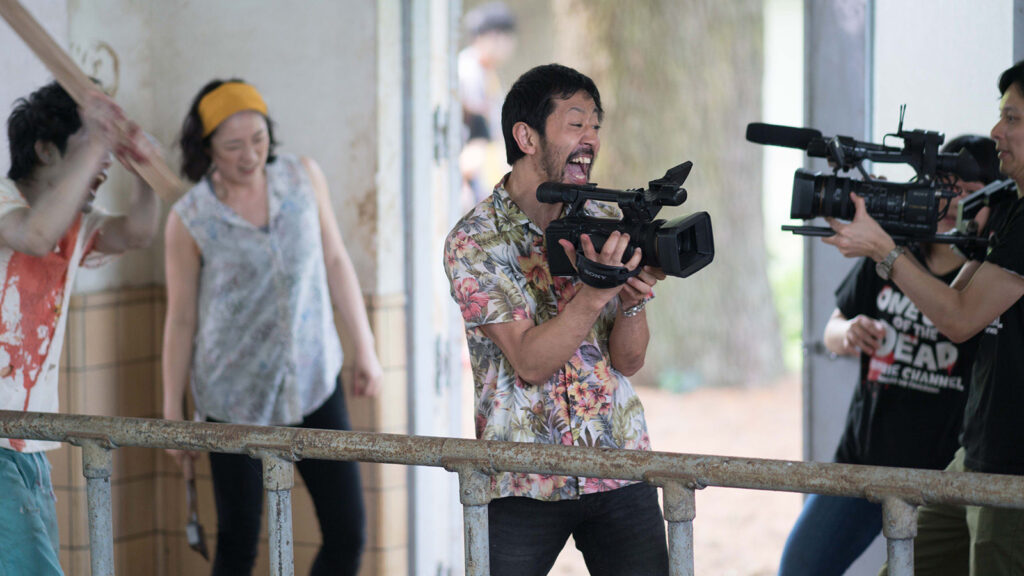 Still Image from One Cut of the Dead. Two Cameramen point their cameras in alternate directions, one towards a Zombie, and one offscreen. 