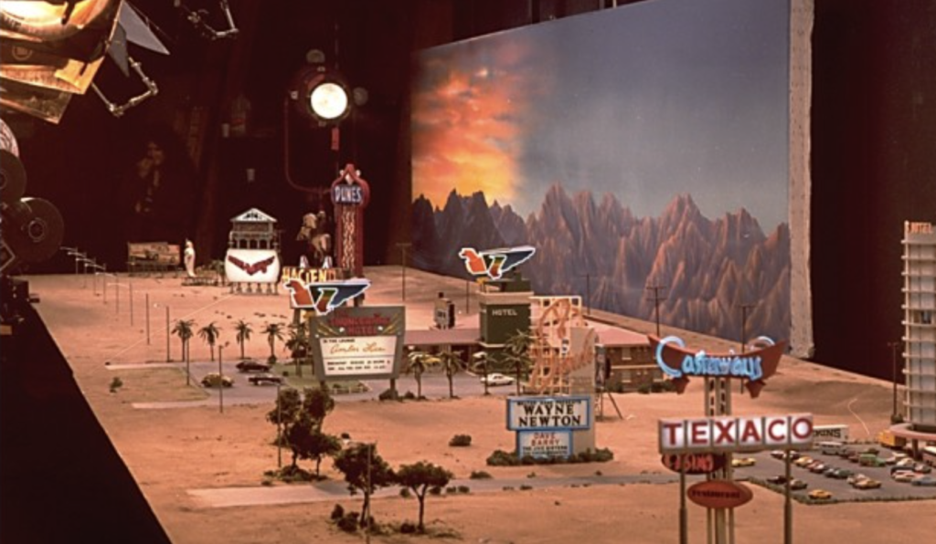 Studio lights illuminate a miniature of the Las Vegas strip, complete with tiny casino signs, tiny trees and a matte painting of mountains at sunset, Hollywood’s American Zoetrope studios,