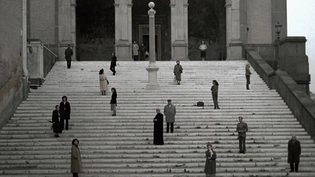 A group of scattered onlookers stand on steps. 