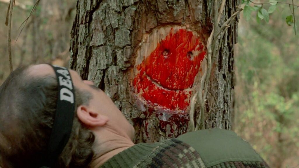 A head coming away from a tree trunk revealing a bloody smiley face from Friday the 13th VI: Jason Lives.