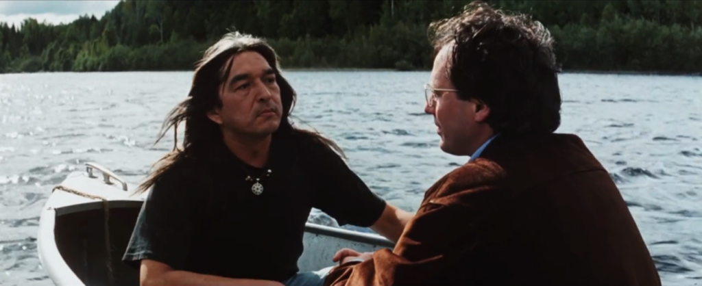 Arthur, a black haired man, sits in a canoe with Maguire, a man with short brown here.