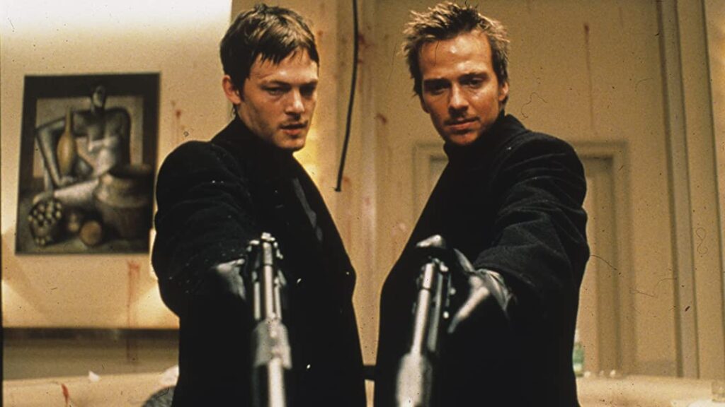 A still from The Boondock Saints. The MacManus Brothers dress in matching black coats and point handguns toward bottom of frame