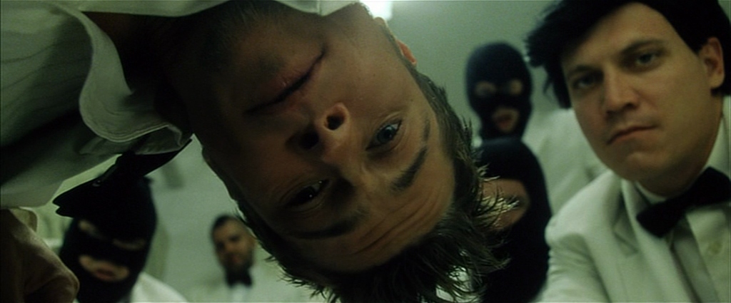 A still from Fight Club. Tyler Durden stoops down close to frame with masked figures behind him