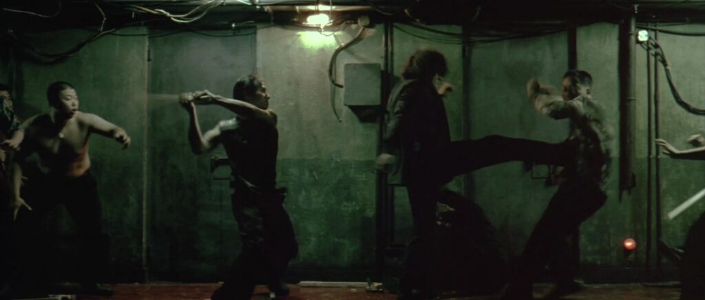 A still from Oldboy. Oh Dae-su kicks a man while an attacker swings a melee weapon from behind.