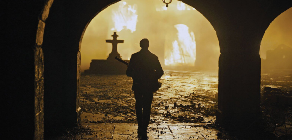 A young man walks toward a burning building. He is obscured by shadows.