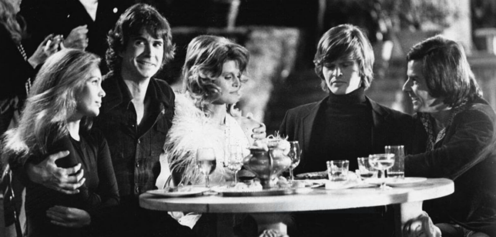 A black and white image of five stylish friends sitting at a table littered with cocktail glasses.