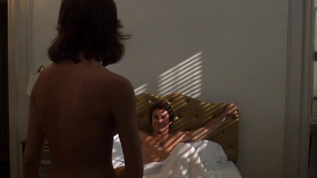 Charlie (Harvey Keitel), in bed, naked, arms stretched across the headboard, face partially obscured by the shadow of window blinds, smiling at Teresa (Amy Robinson), naked and out of focus in the foreground, from Mean Streets (1973).