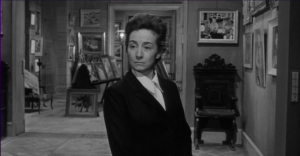 black-and-white image of a white woman with dark hair in a room full of paintings
