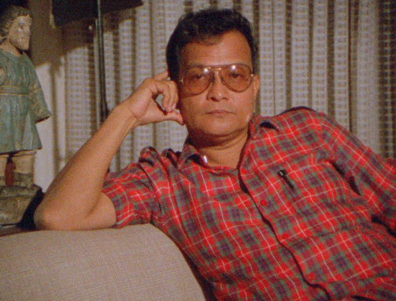 Director Lino Brocka sitting in what looks like a living room with his hand resting on the side of his face and with a neutral expression.