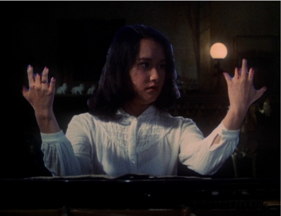 A girl sitting at the piano, looking quizzically at her hands, which are missing several fingers.