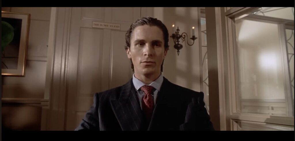 Patrick Bateman sits in a restaurant in front a door with a sign that reads “This is not an exit.”