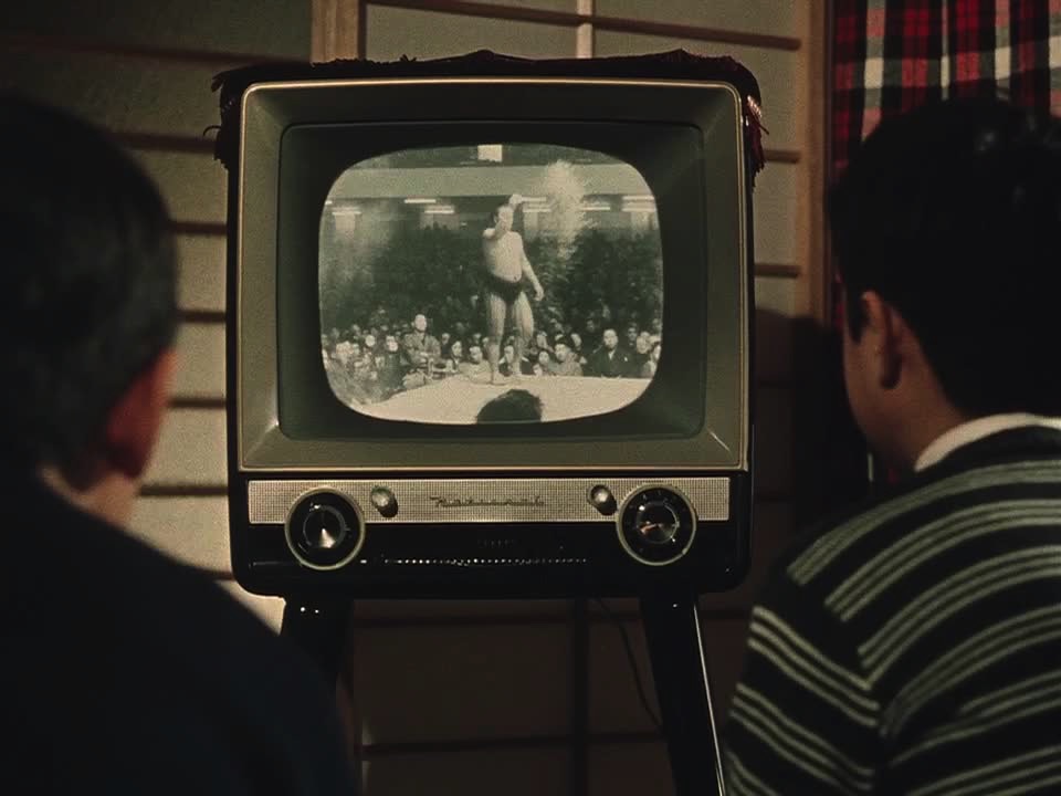 Minoru and his friend watching a sumo wrestling match on TV.