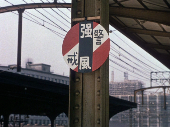 Ozu’s color film Equinox Flower demonstrates his love of the color red, as in this frames which shows a red, white, and blue warning sign in front of a trolley.