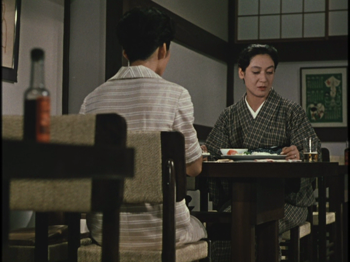 In the Ozu film Late Autumn, the characters of Ayako and Akiko meet for a meal at a restaurant. Akiko is contemplating her delicious beer. There is a table in the foreground and a poster behind the pair.