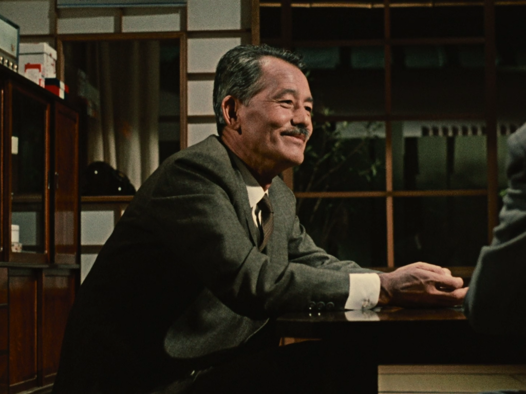 Man in a gray suit sits at a table and smiles