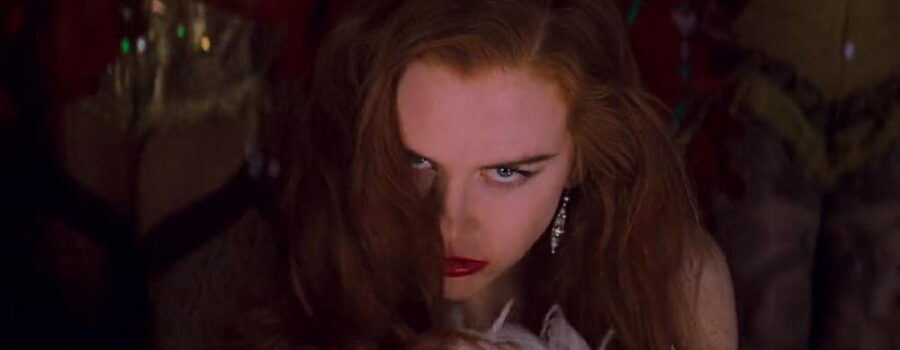 Nicole Kidman, as Satine, a light-skinned woman with loose ginger hair, is gazing at the camera with a look of dangerous seduction on her face.