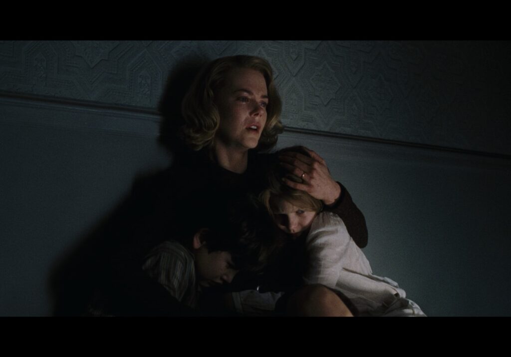 A distraught Nicole Kidman sits against a wall while embracing her two young children.