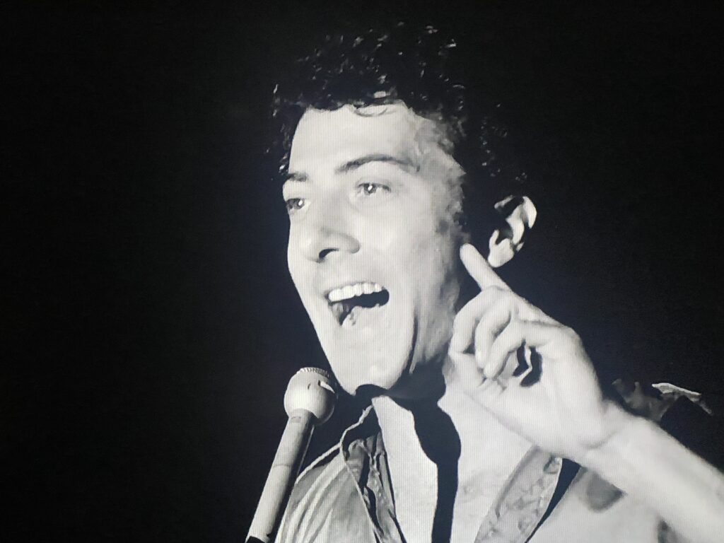 Close up black and white image of a standup comedian performing in nightclub.