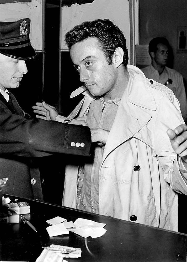 Full body shot of Lenny Bruce being frisked by the police.