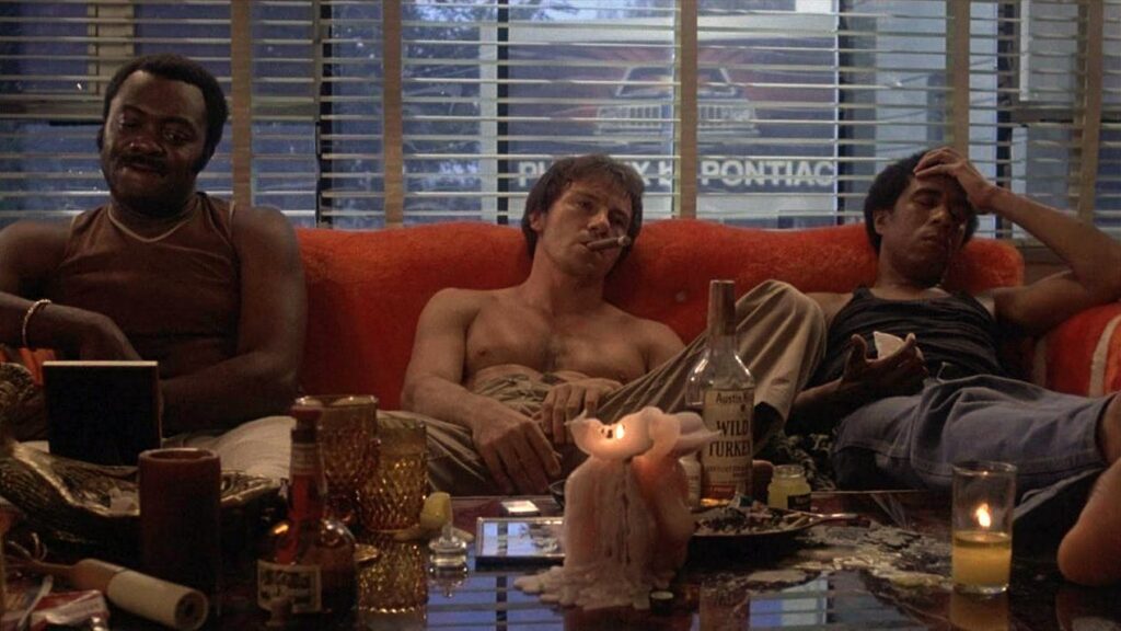 Yaphet Kotto, shirtless Harvey Keitel, and Richard Pryor sit on a red couch appearing hungover after a party in the film Blue Collar.