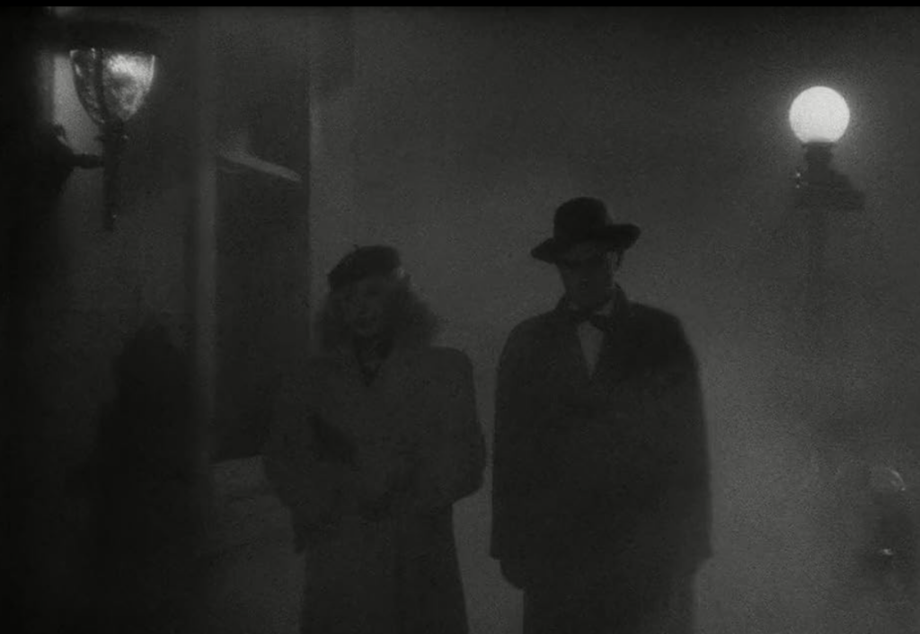 Al and Sue walk through a darkened, foggy city street. 