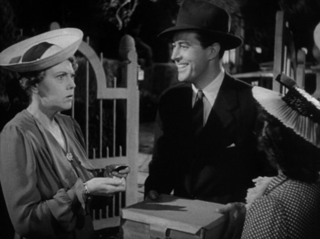 A smiling man wearing a suit and hat holds a cake box, foiling the attempt of two women wearing dresses and hats who tried to take back the cake.
